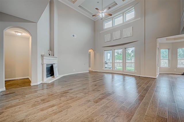 unfurnished living room featuring visible vents, a fireplace with raised hearth, a ceiling fan, wood finished floors, and arched walkways