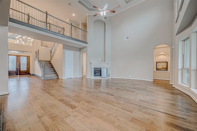 unfurnished living room featuring ceiling fan with notable chandelier, a glass covered fireplace, stairway, light wood finished floors, and baseboards