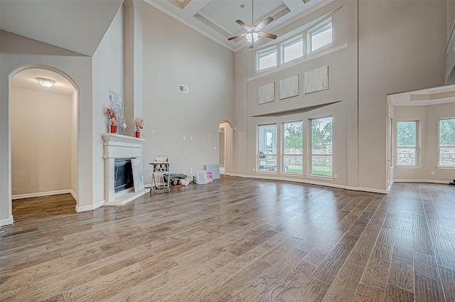 unfurnished living room with a ceiling fan, wood finished floors, visible vents, a fireplace with raised hearth, and arched walkways