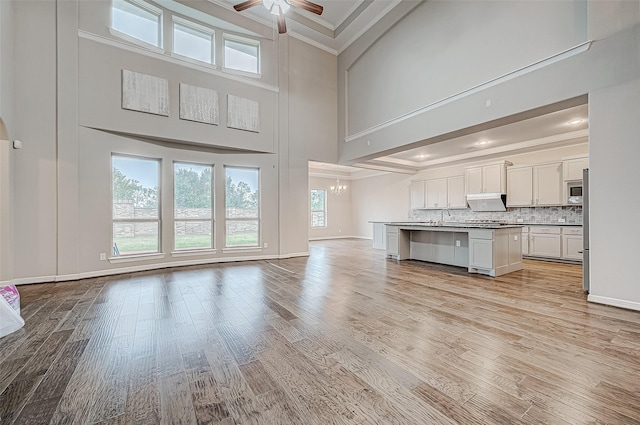 unfurnished living room with ornamental molding, ceiling fan with notable chandelier, a sink, light wood-style floors, and a high ceiling