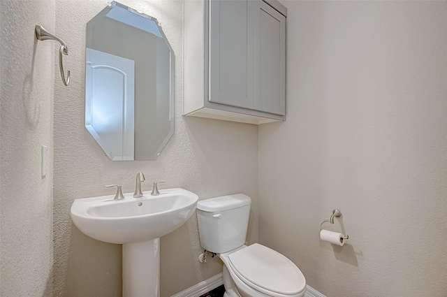 bathroom with toilet, a textured wall, and baseboards