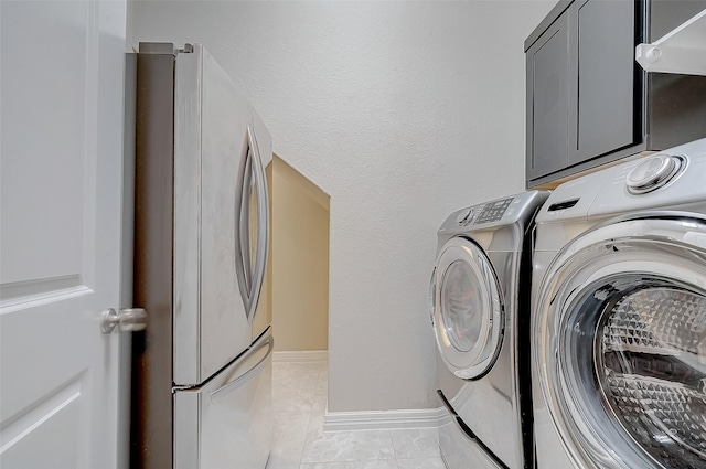 washroom featuring washer and dryer, laundry area, light tile patterned floors, and baseboards