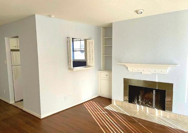 unfurnished living room with baseboards, wood finished floors, and a tiled fireplace