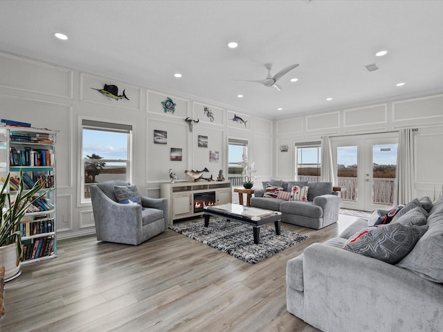 living room with ornamental molding, a decorative wall, a ceiling fan, and light wood-style flooring