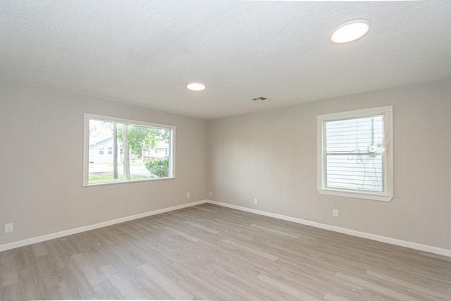 spare room featuring visible vents, baseboards, light wood-style floors, and a textured ceiling