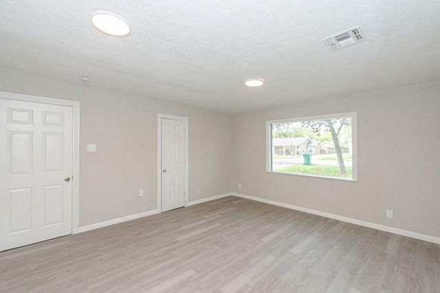 empty room featuring visible vents, a textured ceiling, baseboards, and wood finished floors