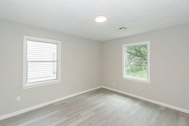 spare room featuring a textured ceiling, baseboards, visible vents, and light wood-type flooring