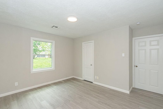 spare room featuring baseboards, light wood-type flooring, and a textured ceiling