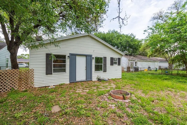 rear view of house with a fire pit, a yard, and fence