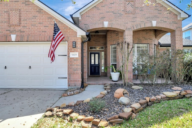 view of exterior entry with brick siding, an attached garage, and driveway