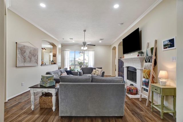 living area featuring wood finished floors, baseboards, a fireplace with raised hearth, arched walkways, and ceiling fan