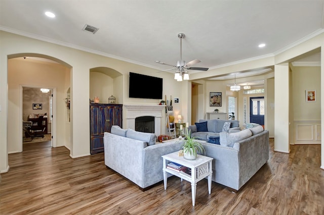 living room featuring visible vents, ornamental molding, a ceiling fan, wood finished floors, and a fireplace