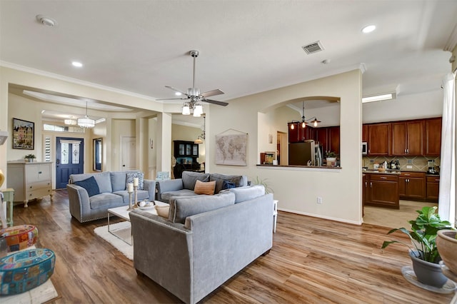 living area with baseboards, ornamental molding, recessed lighting, ceiling fan with notable chandelier, and light wood-style floors