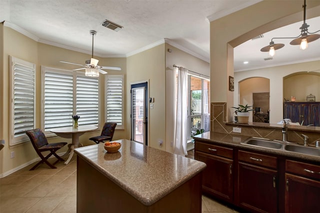 kitchen featuring visible vents, a sink, arched walkways, crown molding, and ceiling fan