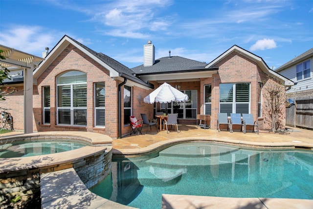 back of house featuring brick siding, a pool with connected hot tub, fence, a chimney, and a patio area