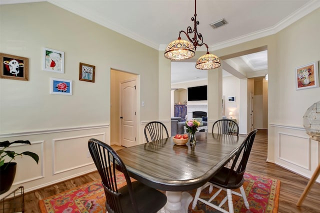 dining room featuring visible vents, dark wood-type flooring, crown molding, wainscoting, and a fireplace