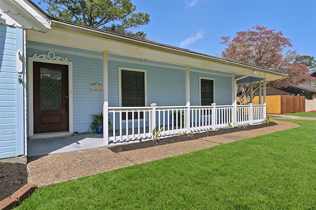 doorway to property featuring a yard, covered porch, and fence