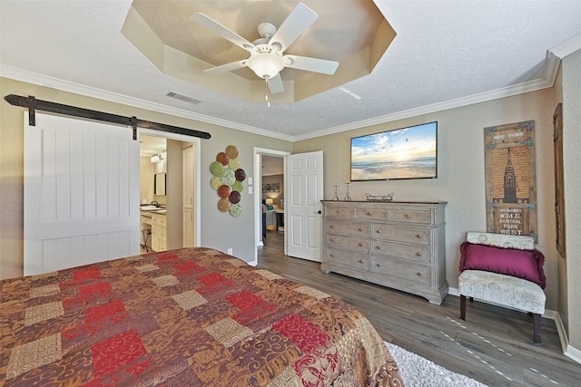 bedroom with wood finished floors, visible vents, a tray ceiling, ornamental molding, and a barn door