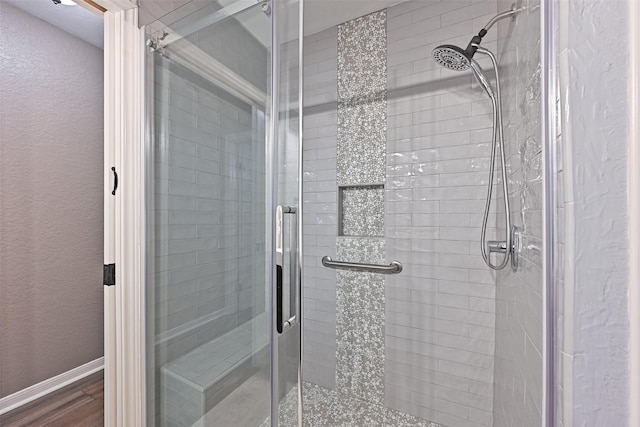 bathroom with a shower stall, wood finished floors, baseboards, and a textured wall