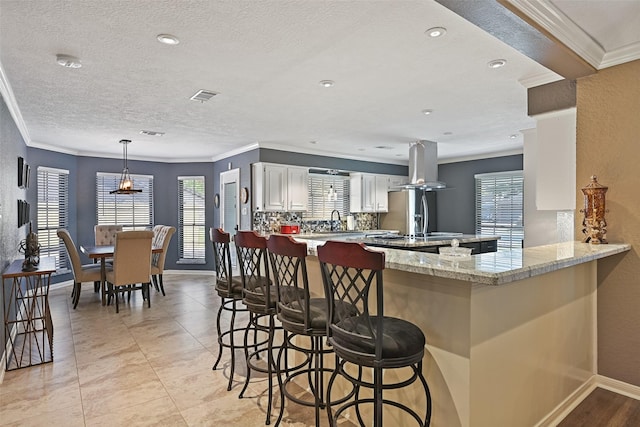 kitchen with visible vents, a peninsula, white cabinets, crown molding, and island range hood