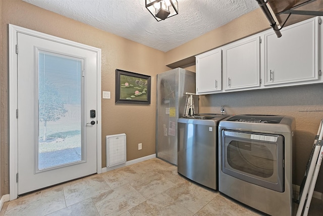 clothes washing area featuring a textured ceiling, washing machine and dryer, cabinet space, baseboards, and a textured wall