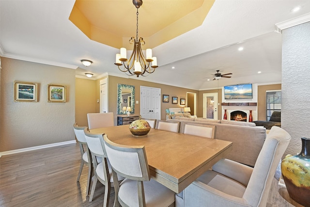 dining area featuring ornamental molding, ceiling fan with notable chandelier, a tray ceiling, wood finished floors, and baseboards