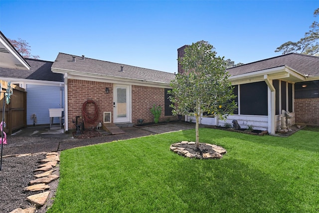 back of house featuring entry steps, a yard, brick siding, and a chimney