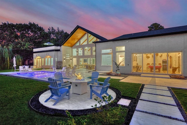 back of property with an outdoor fire pit, a yard, an outdoor pool, a patio area, and brick siding