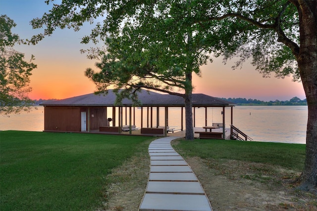 back of property at dusk featuring a water view and a lawn