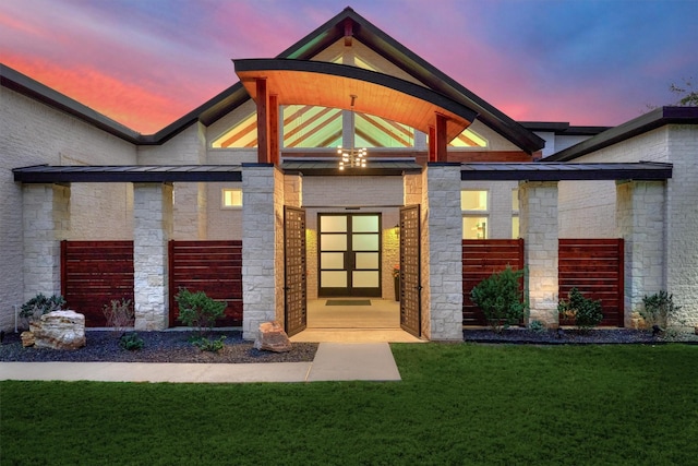 exterior entry at dusk with a yard, brick siding, and stone siding