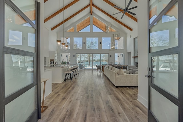 living area featuring ceiling fan with notable chandelier, beam ceiling, wood finished floors, and high vaulted ceiling