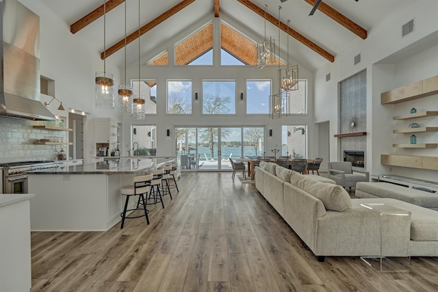 living area featuring visible vents, a fireplace, beamed ceiling, light wood-type flooring, and a chandelier