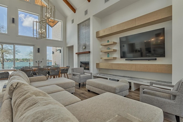 living area with a water view, a notable chandelier, beam ceiling, a tiled fireplace, and wood finished floors