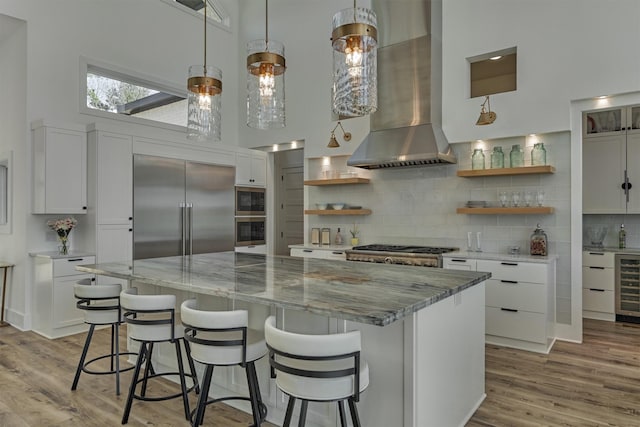 kitchen featuring built in appliances, a towering ceiling, a large island, wall chimney exhaust hood, and open shelves