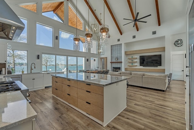 kitchen featuring a fireplace, wall chimney range hood, light stone counters, and light wood-style flooring