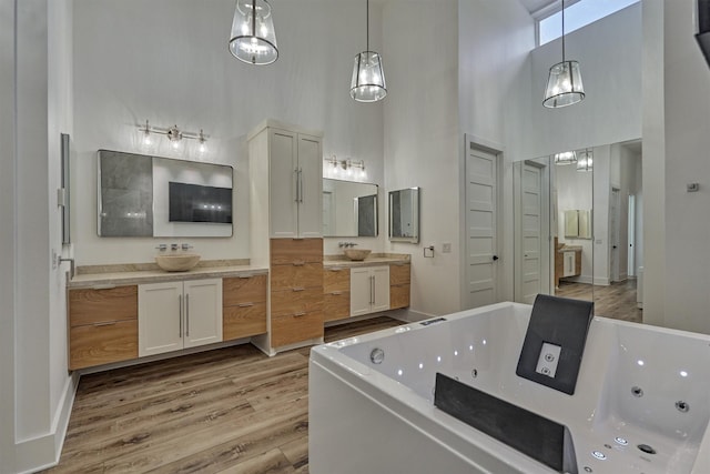 full bathroom featuring a jetted tub, two vanities, a towering ceiling, and wood finished floors