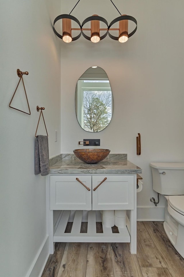 half bath featuring vanity, toilet, wood finished floors, and baseboards