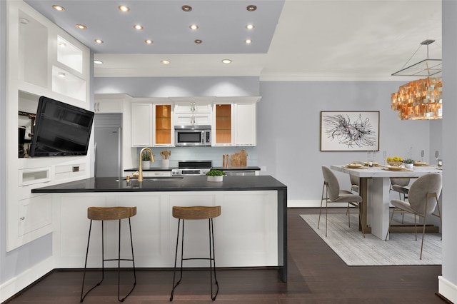 kitchen with dark countertops, a sink, stainless steel appliances, white cabinetry, and dark wood-style flooring