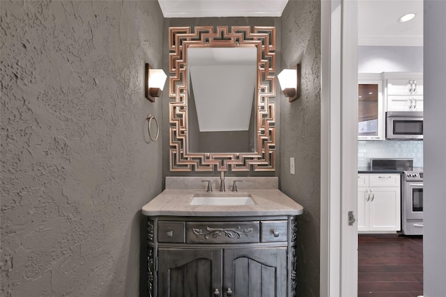 bathroom featuring ornamental molding, wood finished floors, decorative backsplash, vanity, and a textured wall