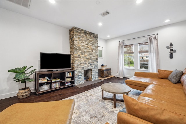 living room with visible vents, a stone fireplace, and wood finished floors