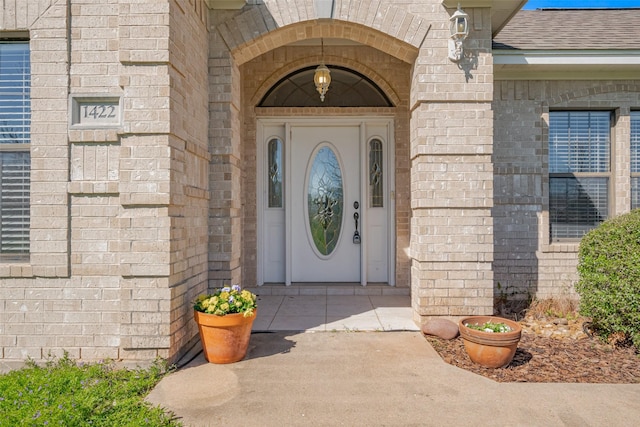 entrance to property with brick siding and a shingled roof