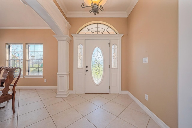 foyer entrance with crown molding, light tile patterned floors, baseboards, and ornate columns