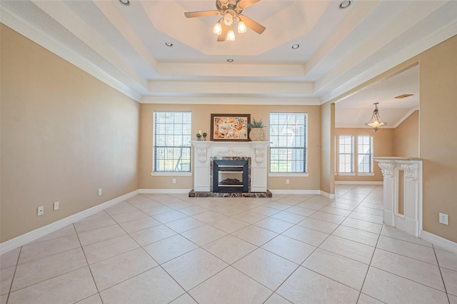 unfurnished living room with a high end fireplace, ceiling fan, baseboards, a tray ceiling, and light tile patterned floors