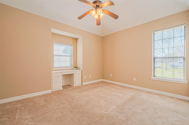 spare room with a ceiling fan, light colored carpet, baseboards, and built in study area