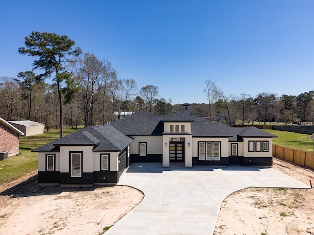 view of front facade featuring stucco siding, french doors, roof with shingles, and fence