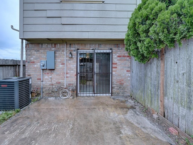 view of exterior entry featuring brick siding, central AC, and fence