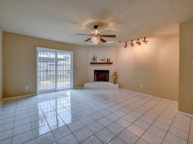 unfurnished living room featuring a brick fireplace, baseboards, ceiling fan, light tile patterned flooring, and a textured ceiling