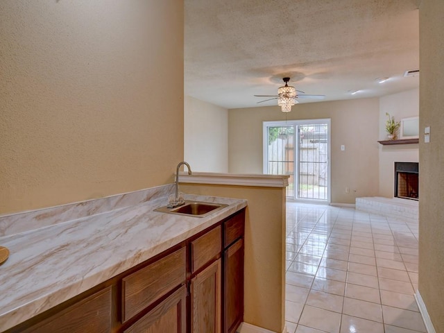 kitchen featuring brown cabinetry, light countertops, a fireplace, light tile patterned flooring, and a sink