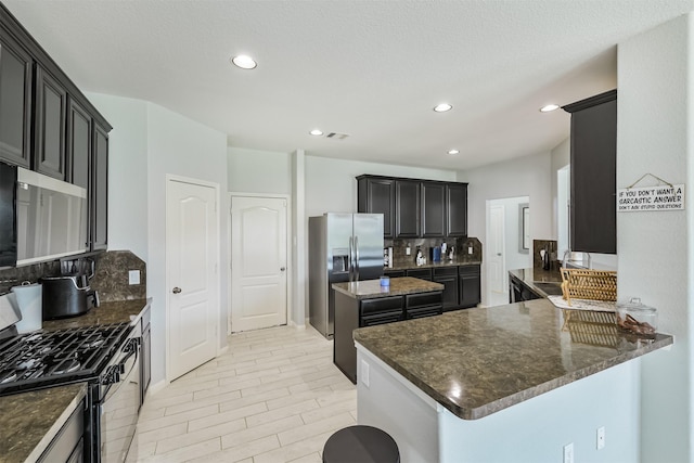 kitchen featuring dark stone counters, recessed lighting, stainless steel appliances, decorative backsplash, and a center island