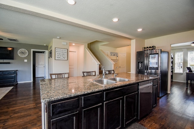 kitchen featuring dark cabinetry, visible vents, an island with sink, stainless steel appliances, and a sink